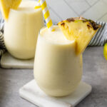 Creamy pineapple banana smoothie with Greek yogurt in two glasses, garnished with pineapple wedges.