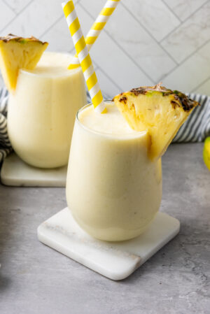 Creamy pineapple banana smoothie with Greek yogurt in two glasses, garnished with pineapple wedges.