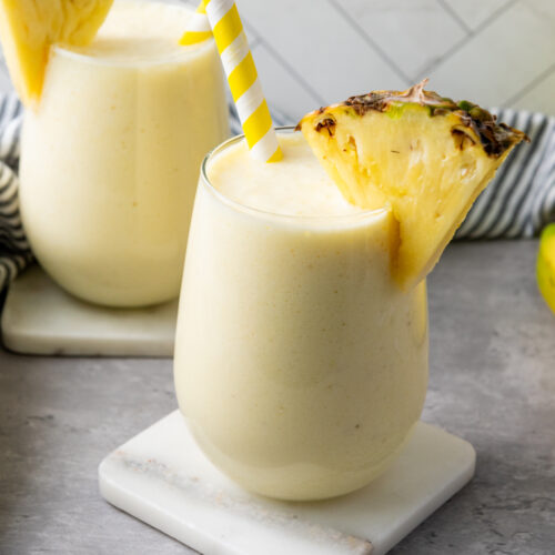 Creamy pineapple banana smoothie with Greek yogurt in two glasses, garnished with pineapple wedges.