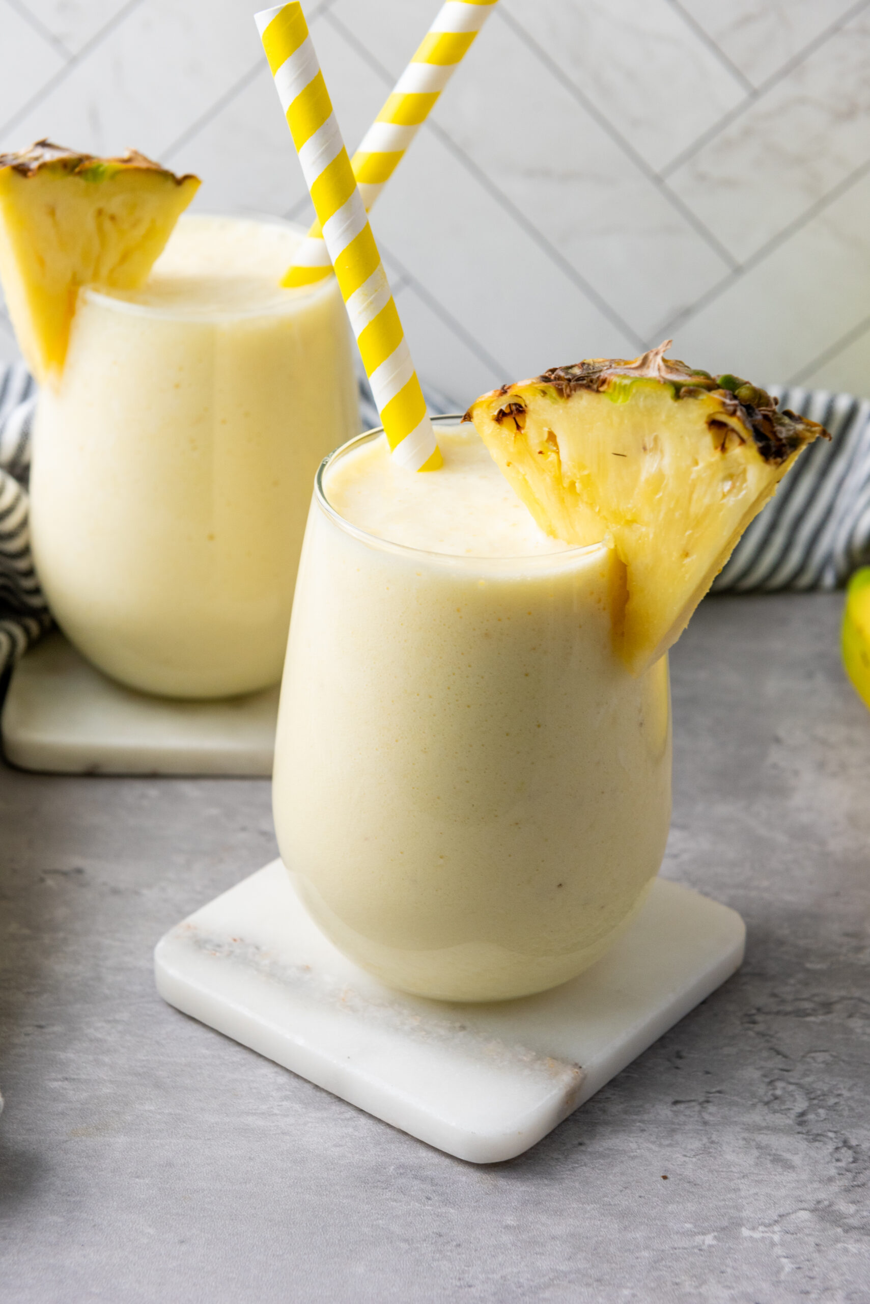 Creamy pineapple banana smoothie with Greek yogurt in two glasses, garnished with pineapple wedges.
