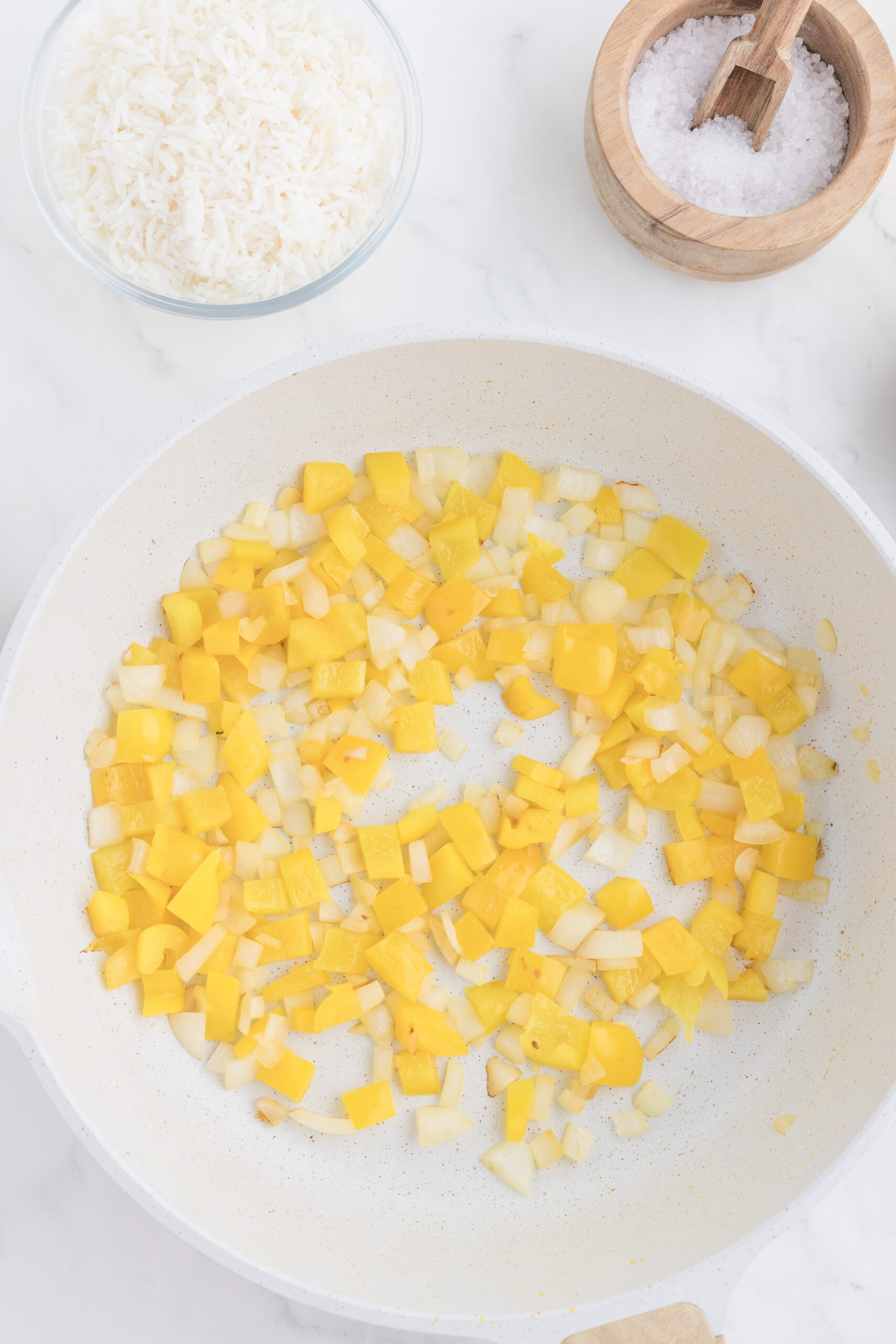Diced yellow onion and bell pepper softening in a skillet.