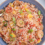 Cajun chicken sausage and rice casserole garnished with sliced green onions in a serving bowl.