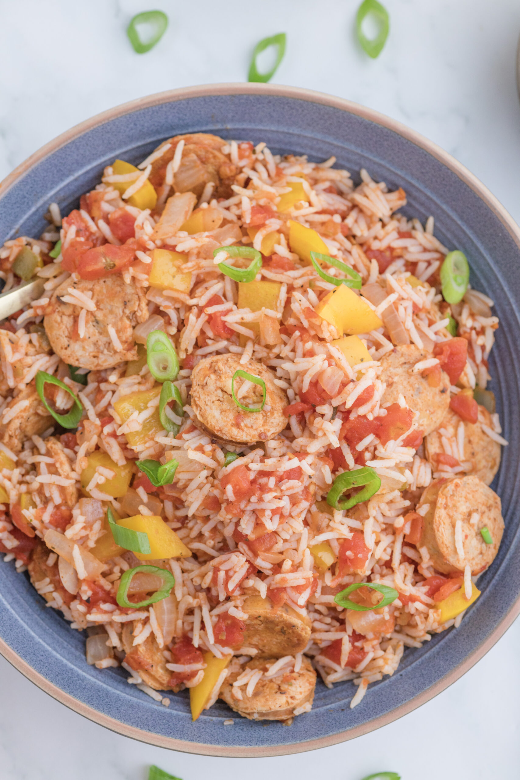 Cajun chicken sausage and rice casserole garnished with sliced green onions in a serving bowl.