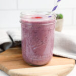 Triple berry smoothie in a glass jar with a striped straw.