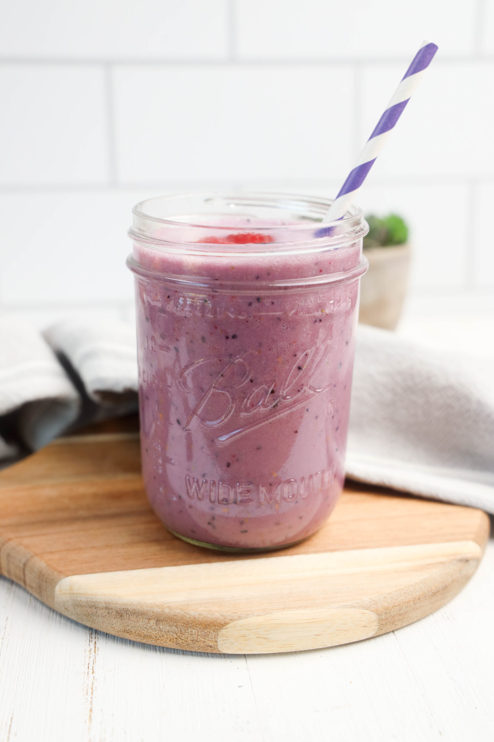 Triple berry smoothie in a glass jar with a striped straw.