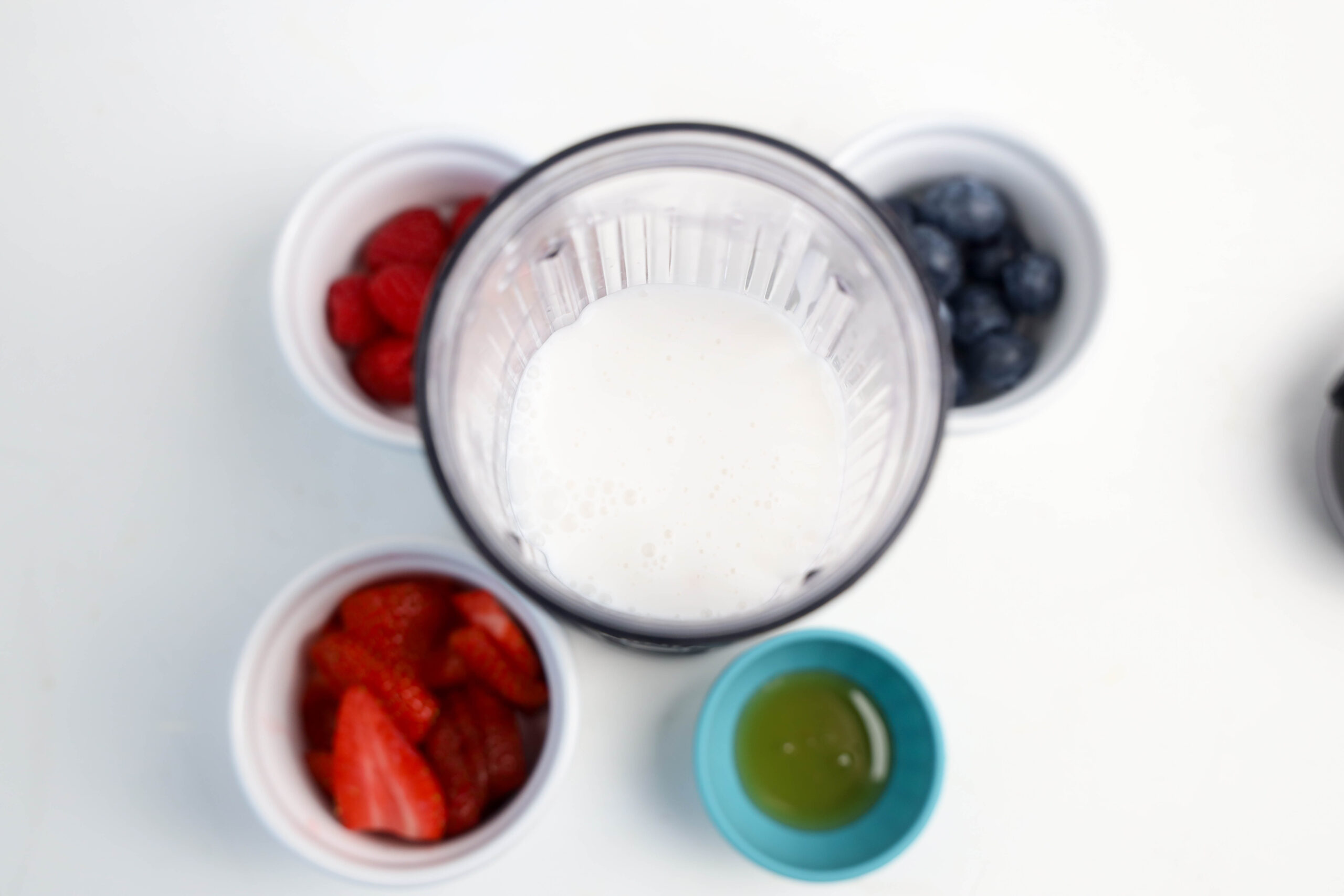 Milk poured into a personal blender with berries and honey nearby.