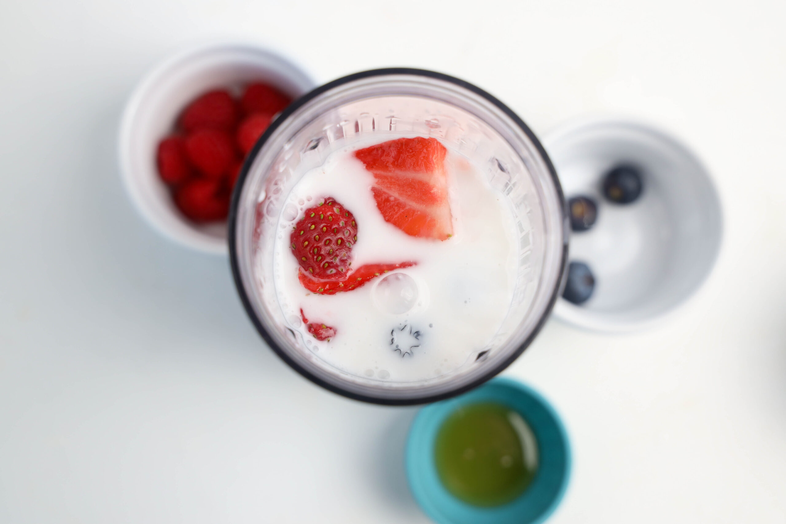 Sliced strawberries added to milk in a personal blender.