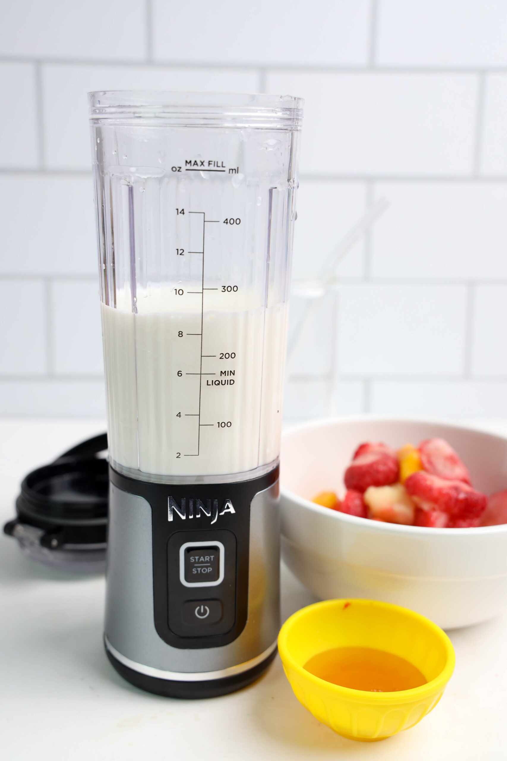 Milk in a personal blender with frozen tropical fruit and honey nearby.
