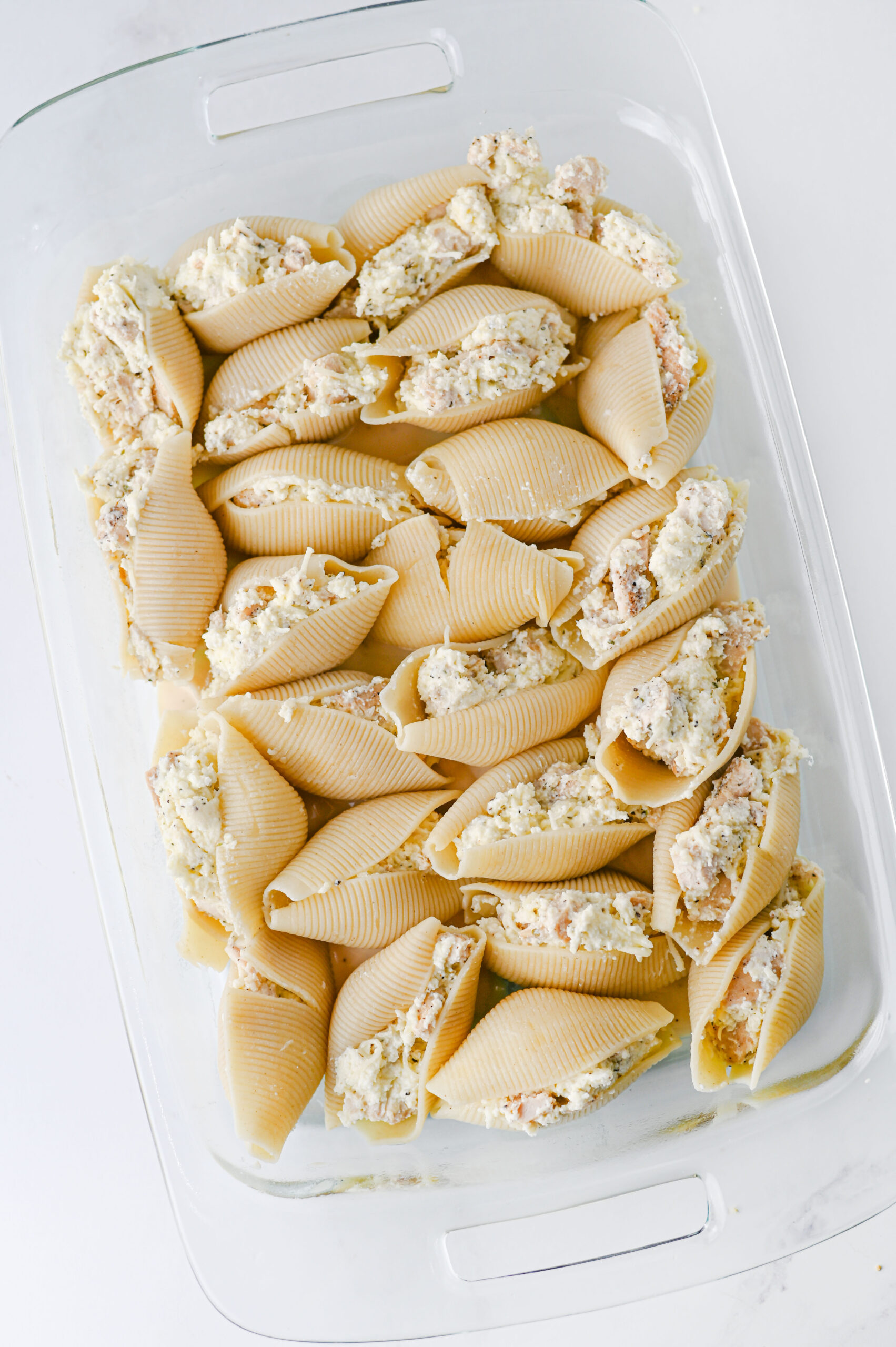 Jumbo pasta shells filled with chicken and ricotta in a baking dish.