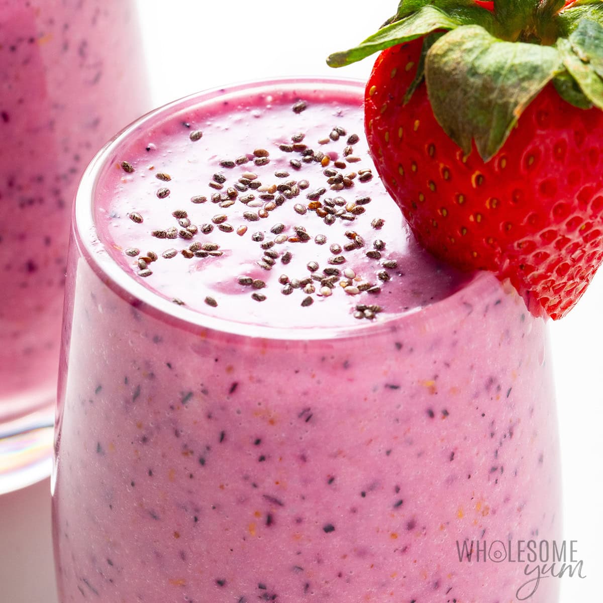 A glass of pink berry smoothie topped with chia seeds, garnished with a fresh strawberry on the rim—it’s one of our favorite high-protein smoothie recipes perfect for a nutritious start to your day.