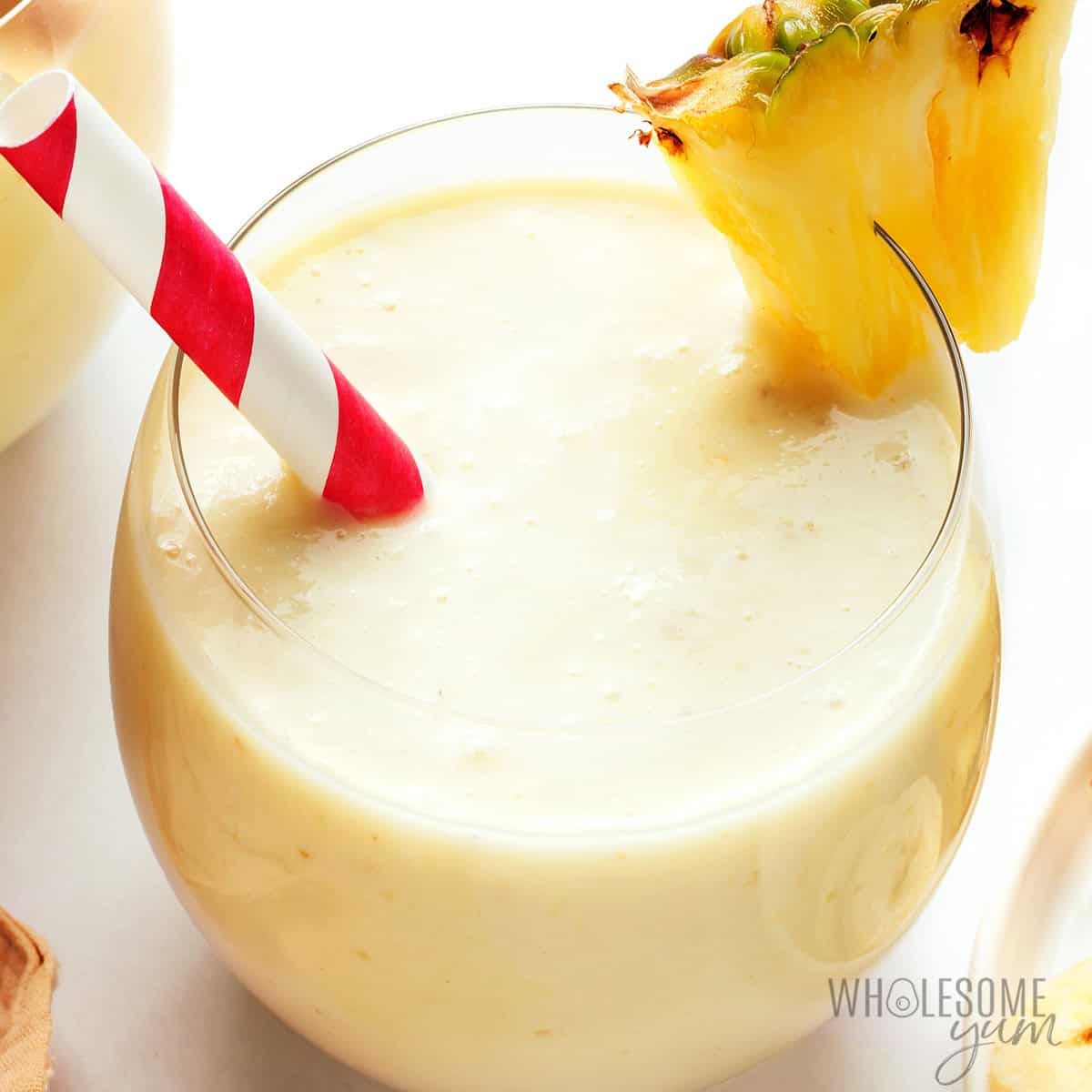 Glass of creamy yellow smoothie with a red and white striped straw and a pineapple wedge garnish on the rim—a delicious example of fruit smoothies perfect for anyone looking to try refreshing new fruit smoothie recipes.