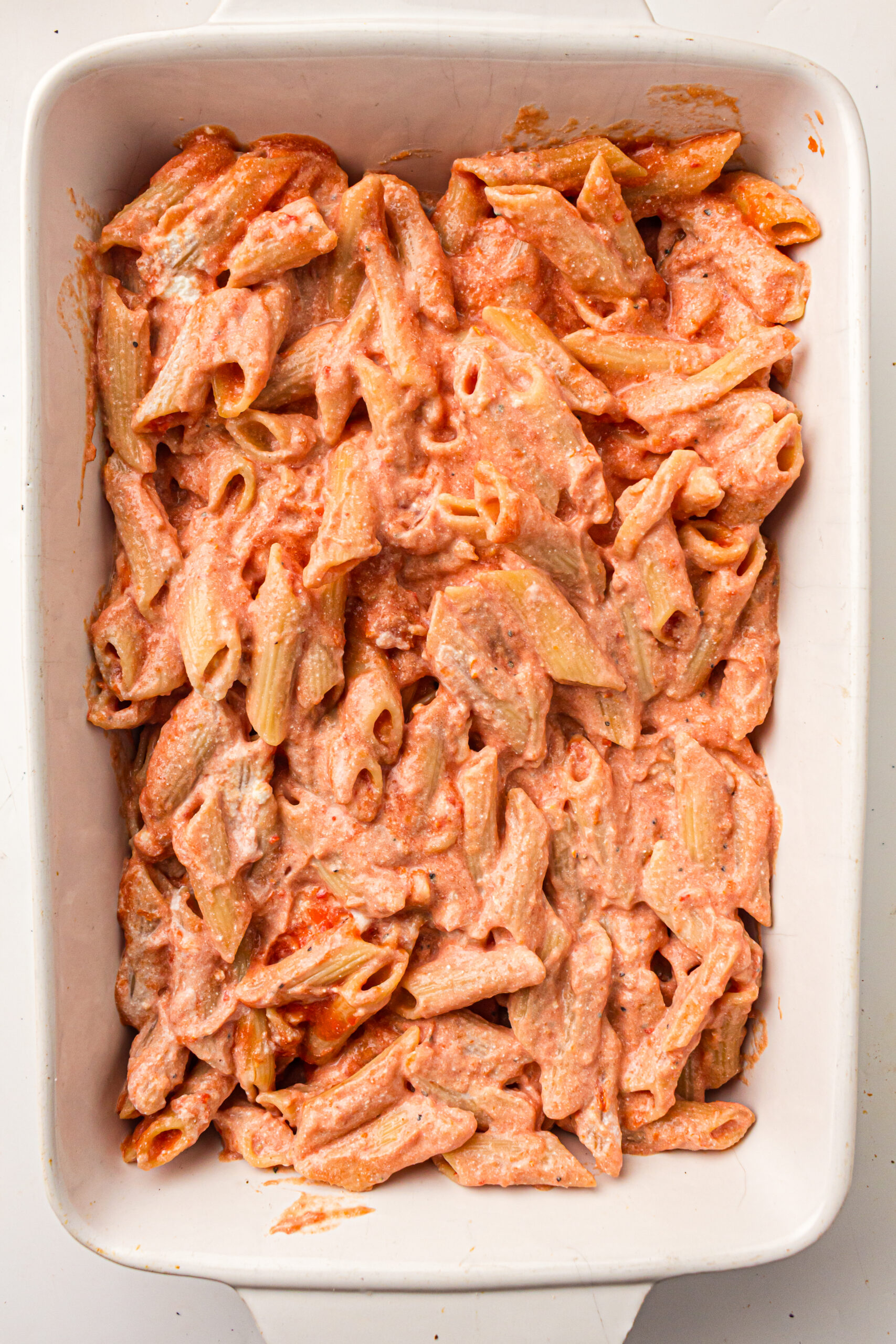 Pasta coated with marinara and ricotta in a greased baking dish.