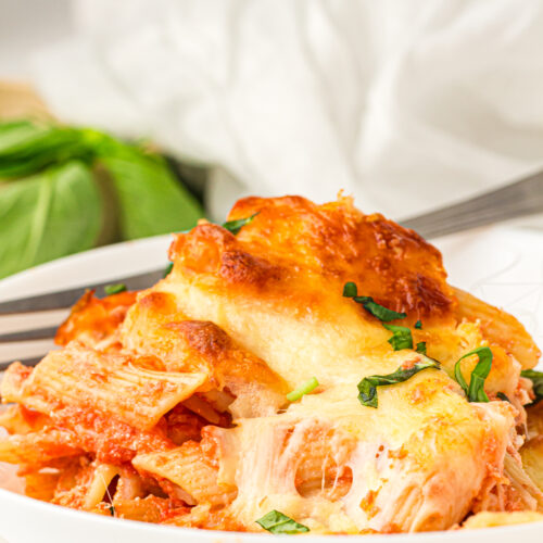 Cheesy baked ziti served in a white bowl with fresh basil.