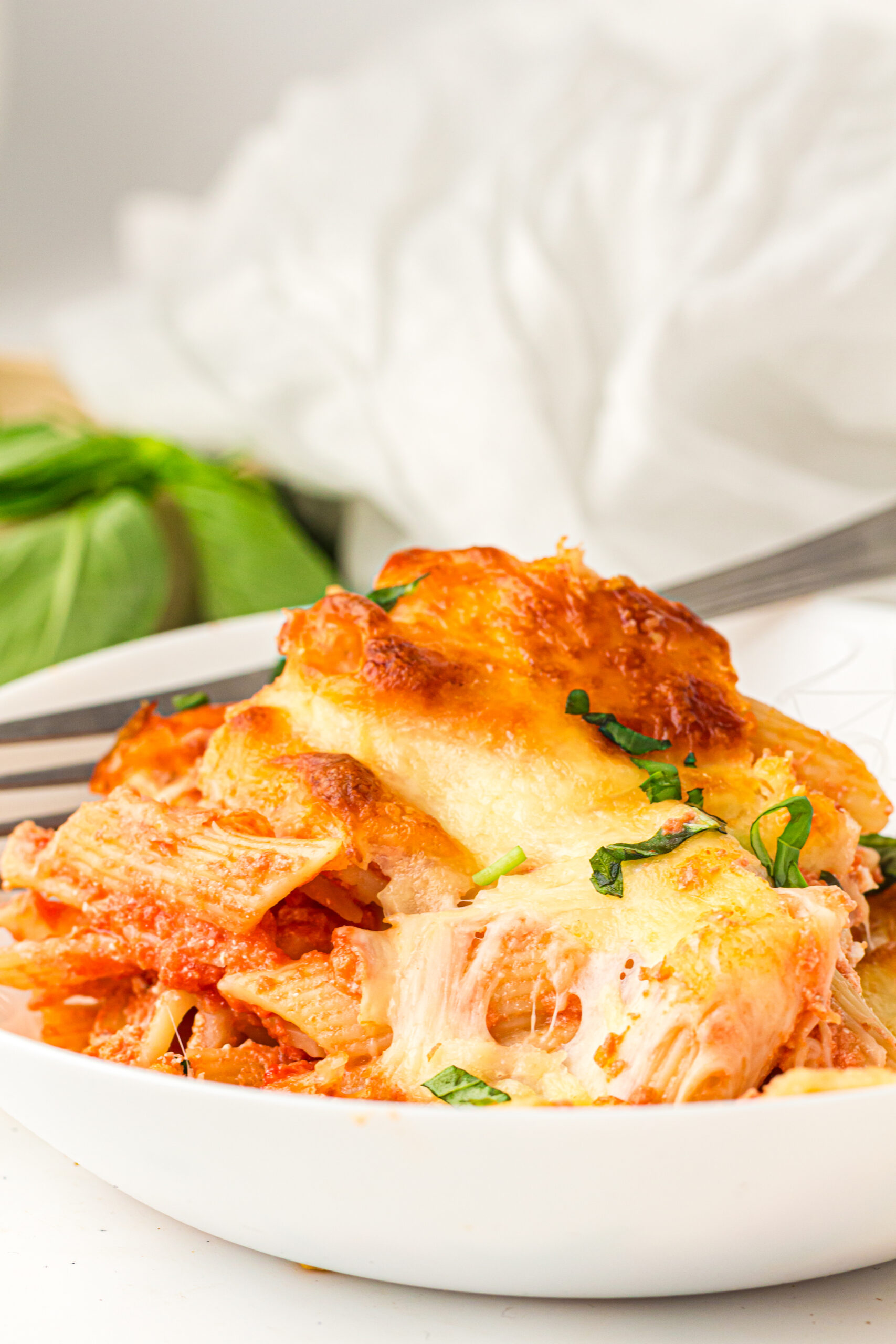 Cheesy baked ziti served in a white bowl with fresh basil.