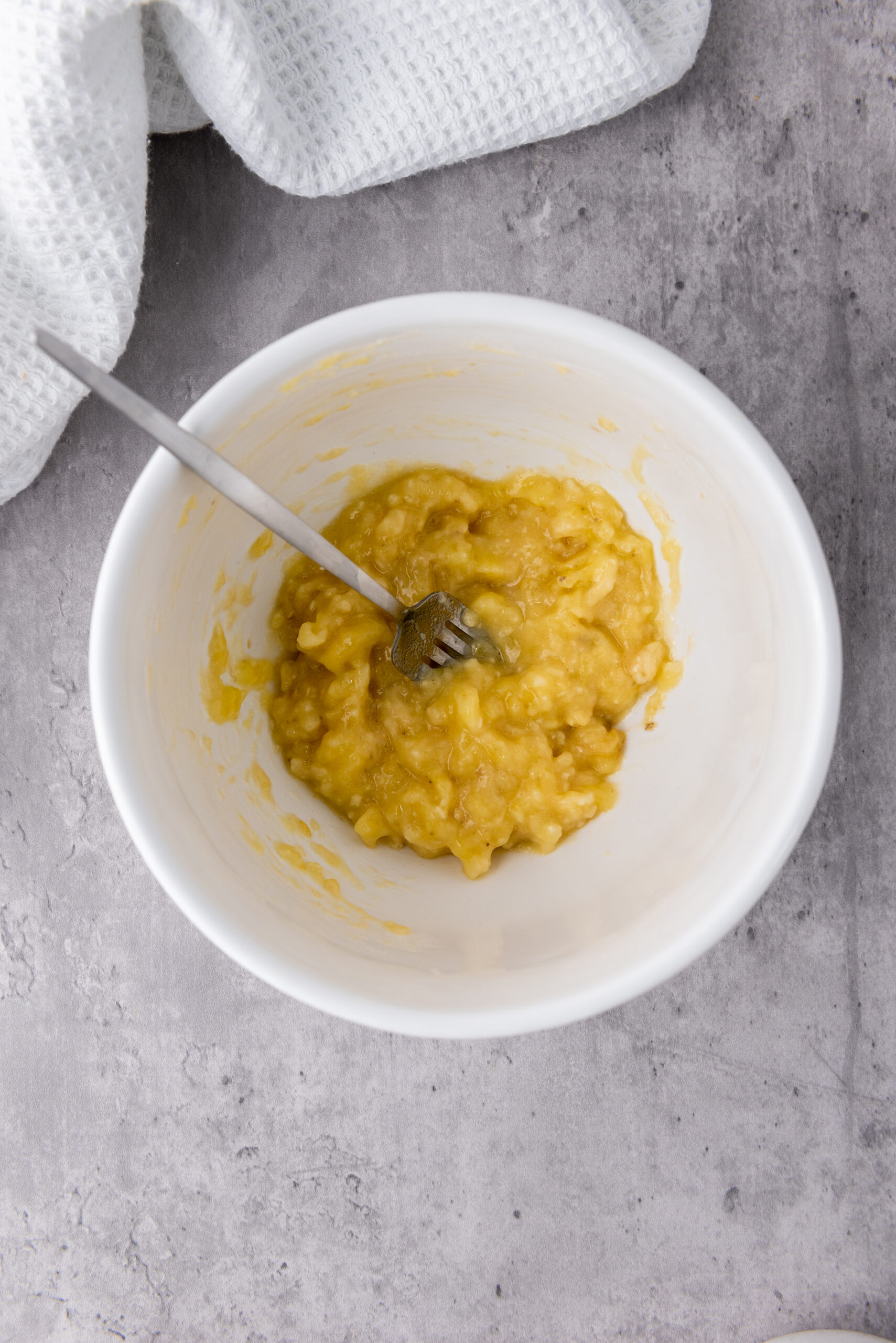 Ripe banana mashed in a white mixing bowl for granola cups.