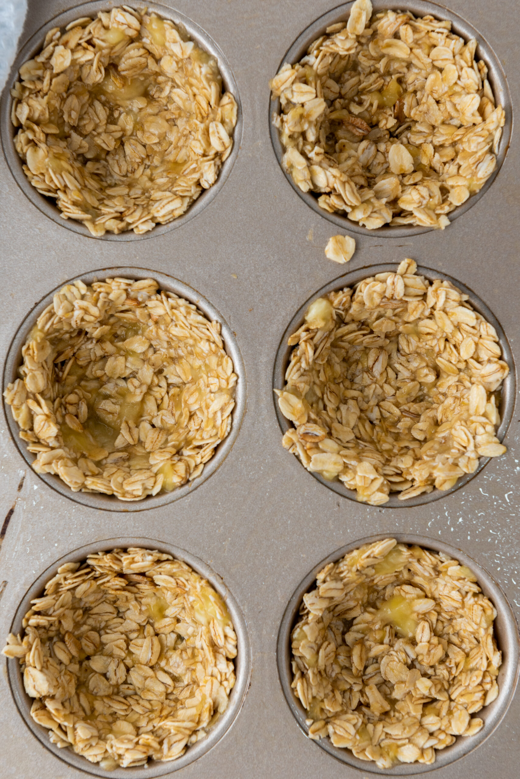 Oat mixture pressed into six muffin cups to form granola cup shells.