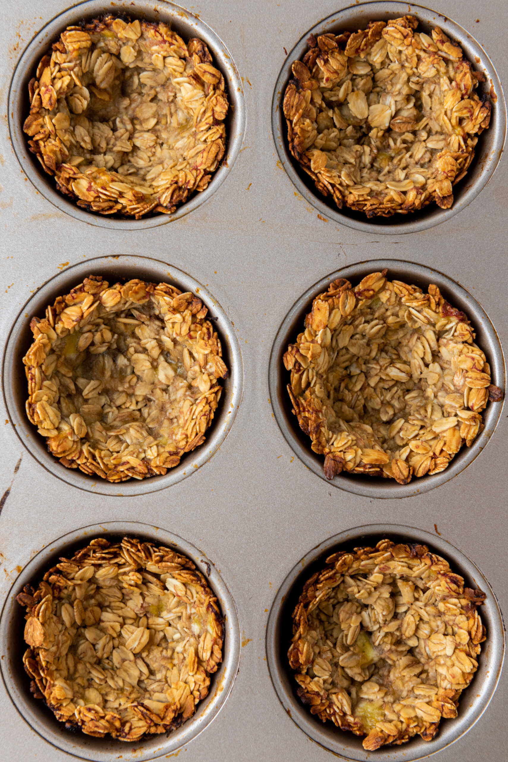 Golden baked granola cups cooling in a muffin tin.