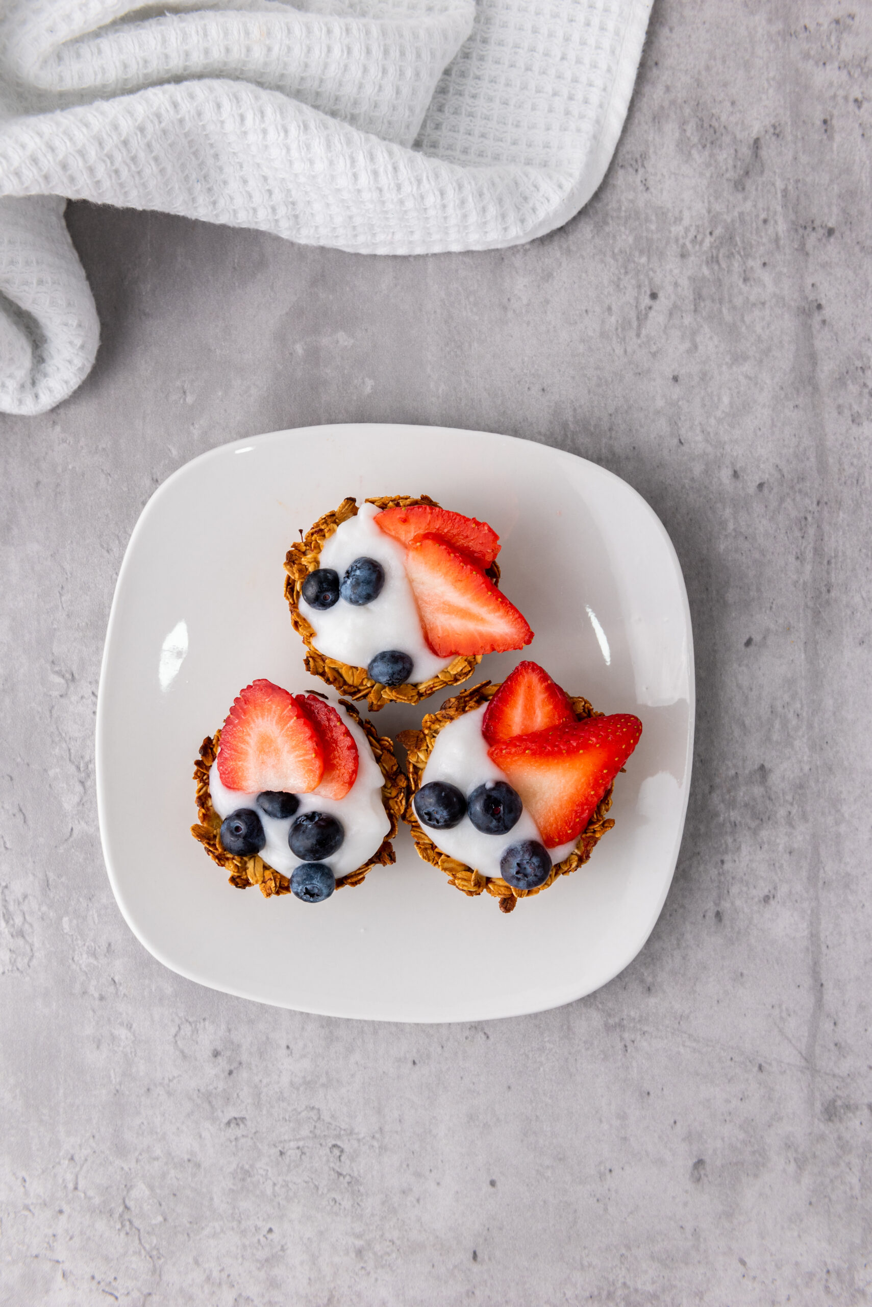 Three granola cups filled with yogurt and topped with strawberries and blueberries.