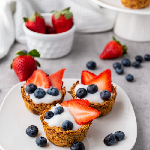 Three granola cups filled with yogurt, strawberries, and blueberries.