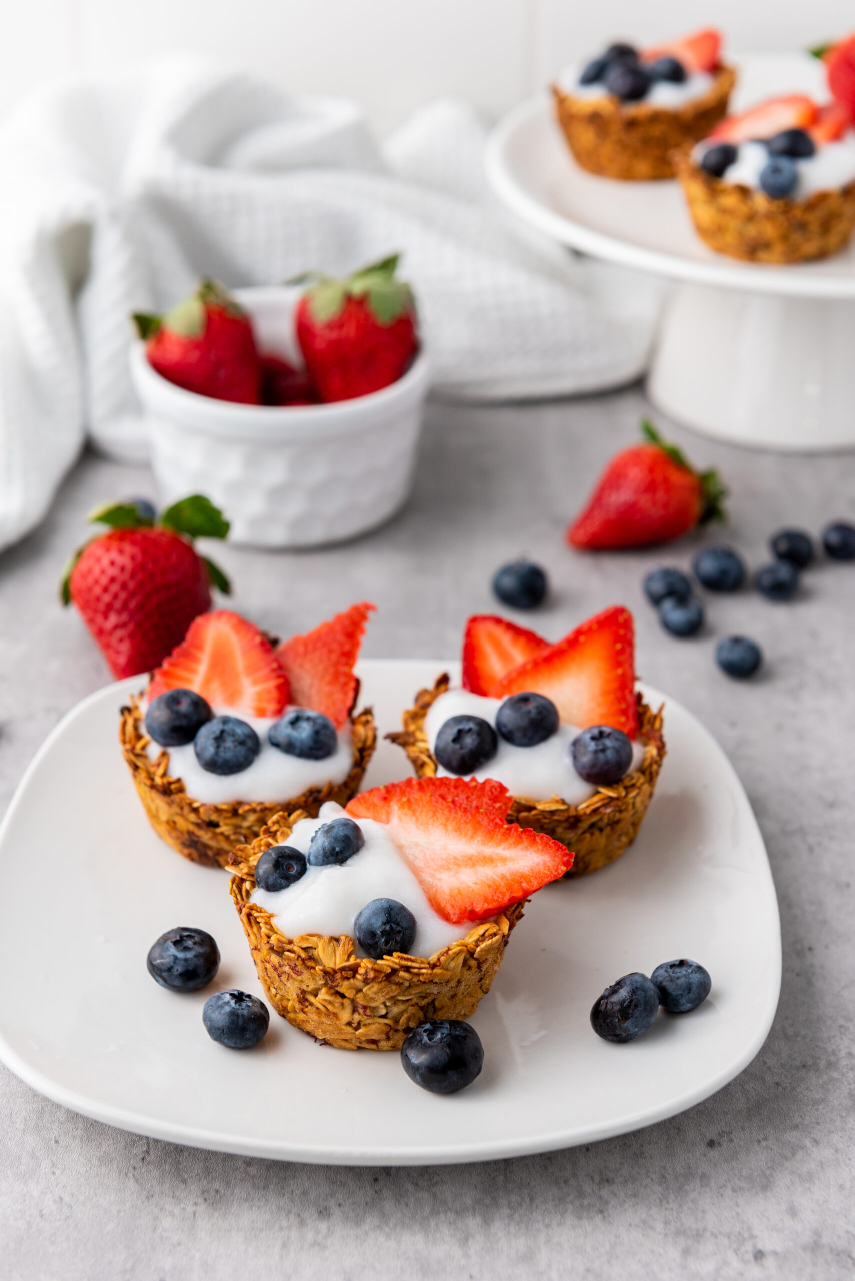 Three granola cups filled with yogurt, strawberries, and blueberries.