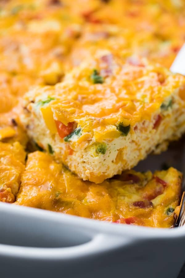 A close-up of a cheesy breakfast casserole with chopped vegetables, cut into squares and served from a baking dish—perfect for hoco brunch or anyone searching for delicious brunch food ideas.
