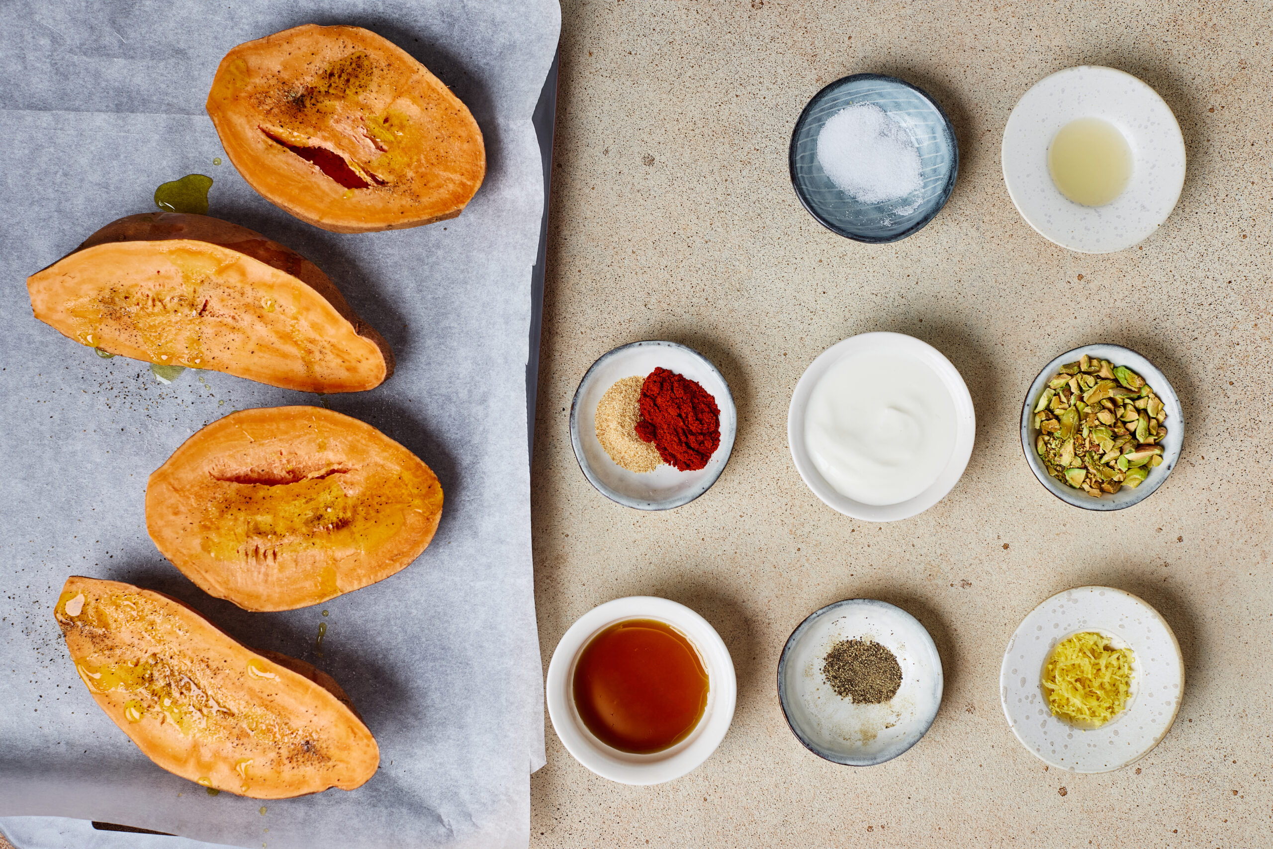 Sweet potato halves brushed with olive oil and seasoned on a parchment-lined baking sheet.