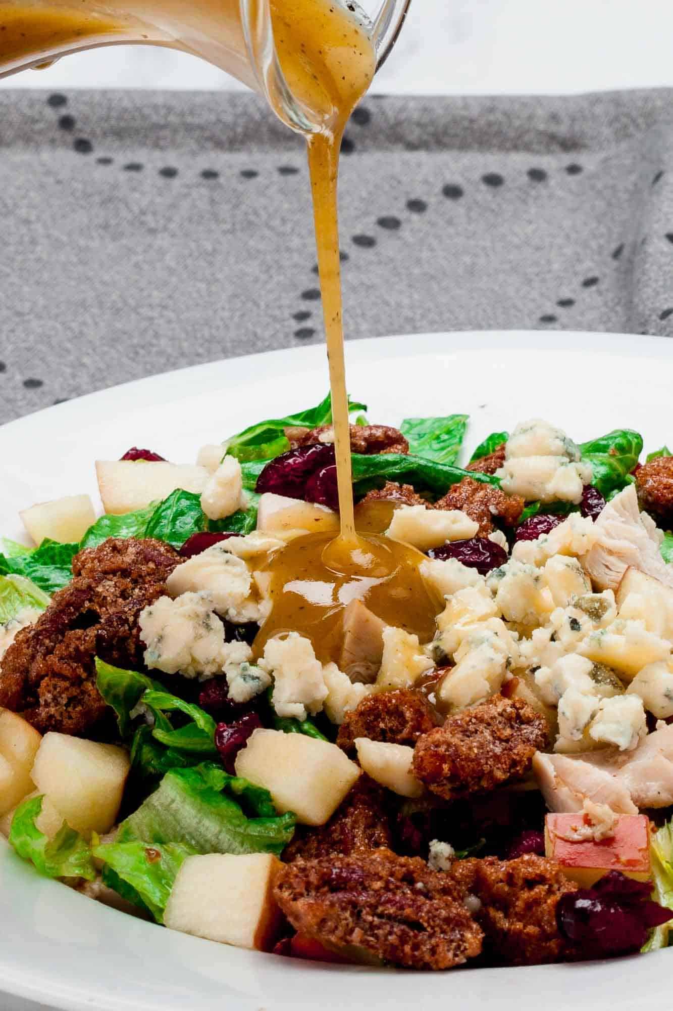 Dressing is poured over a fresh Thanksgiving salad of greens, apples, cranberries, blue cheese, and pecans.