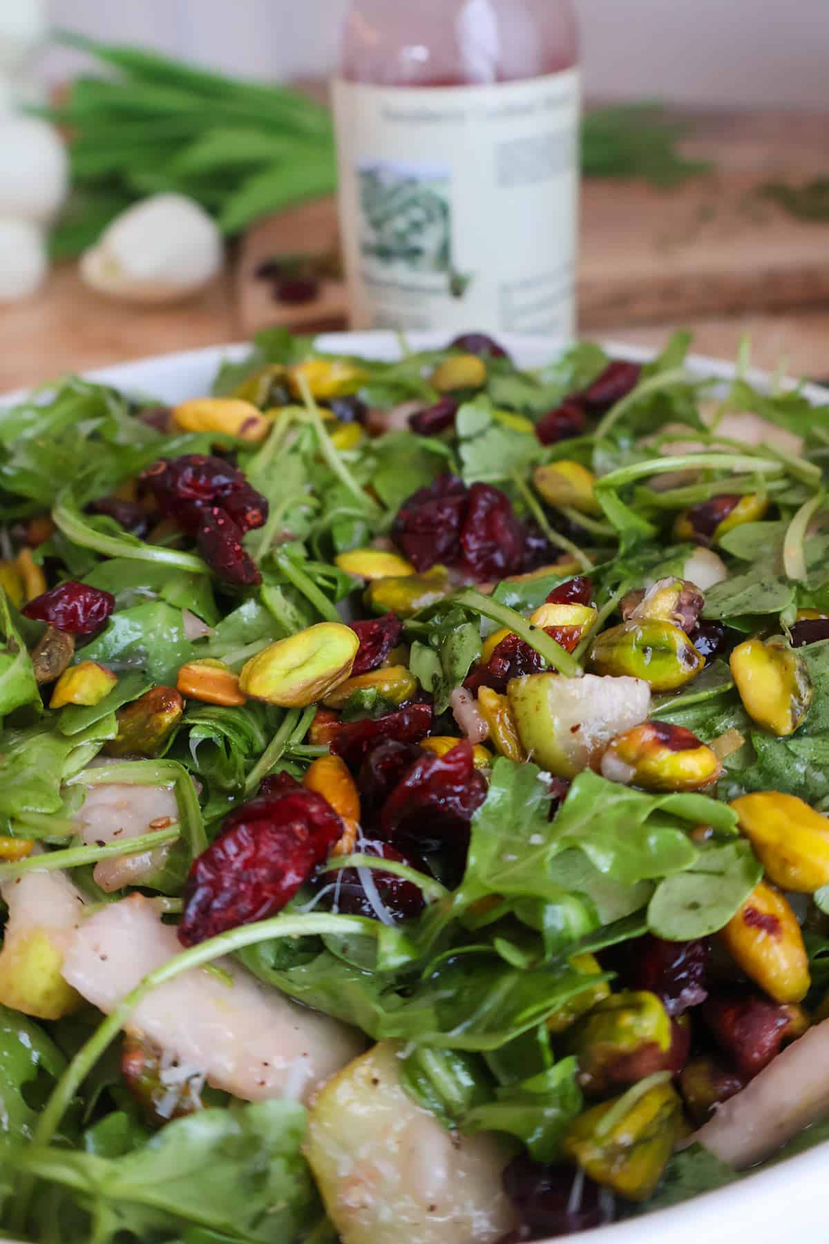 A fresh salad of arugula, dried cranberries, and shelled pistachios in a white bowl, perfect for healthy Thanksgiving recipes.