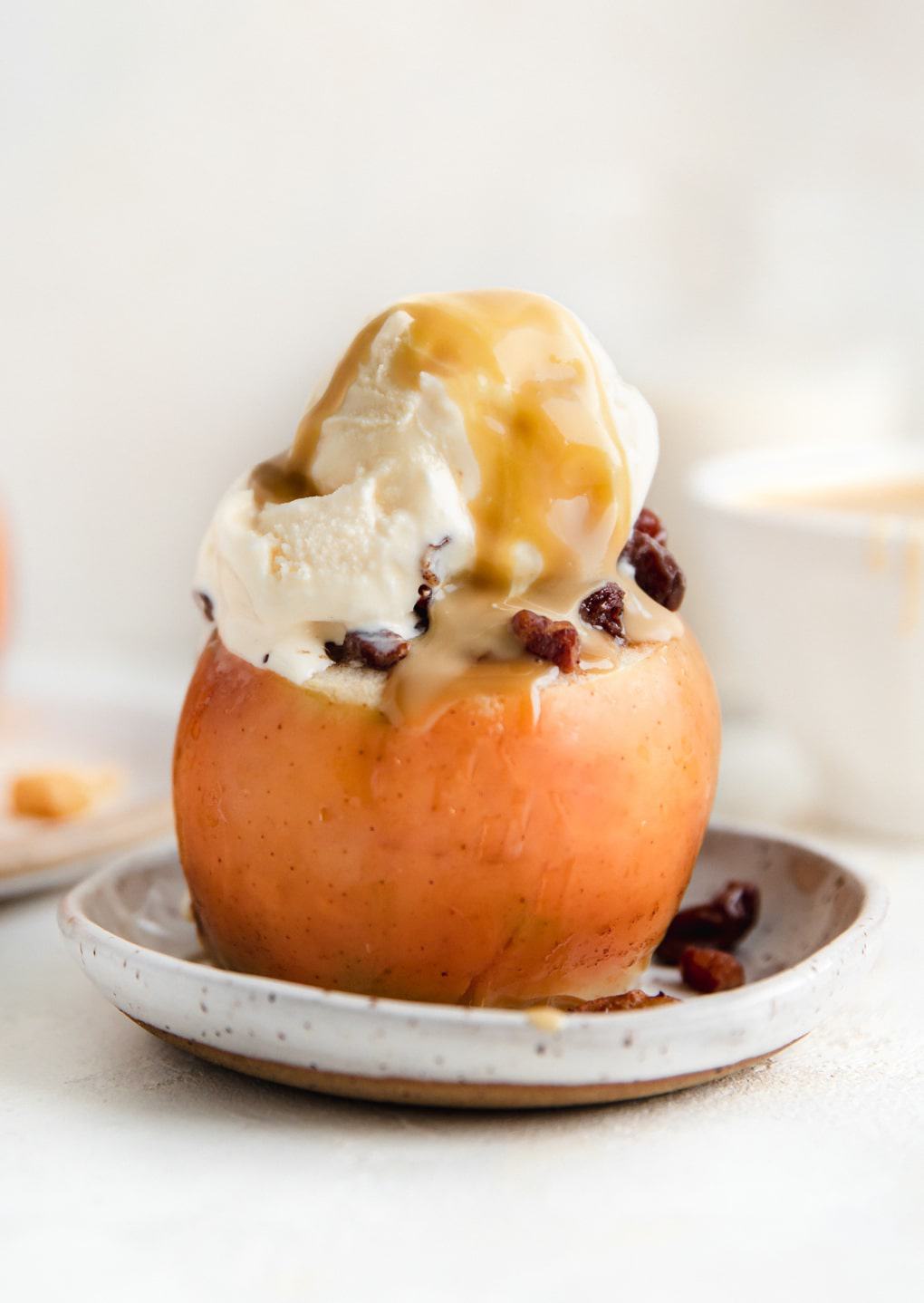 Baked apple topped with a scoop of vanilla ice cream, caramel sauce, and chopped nuts on a small plate, perfect for healthy Thanksgiving desserts.