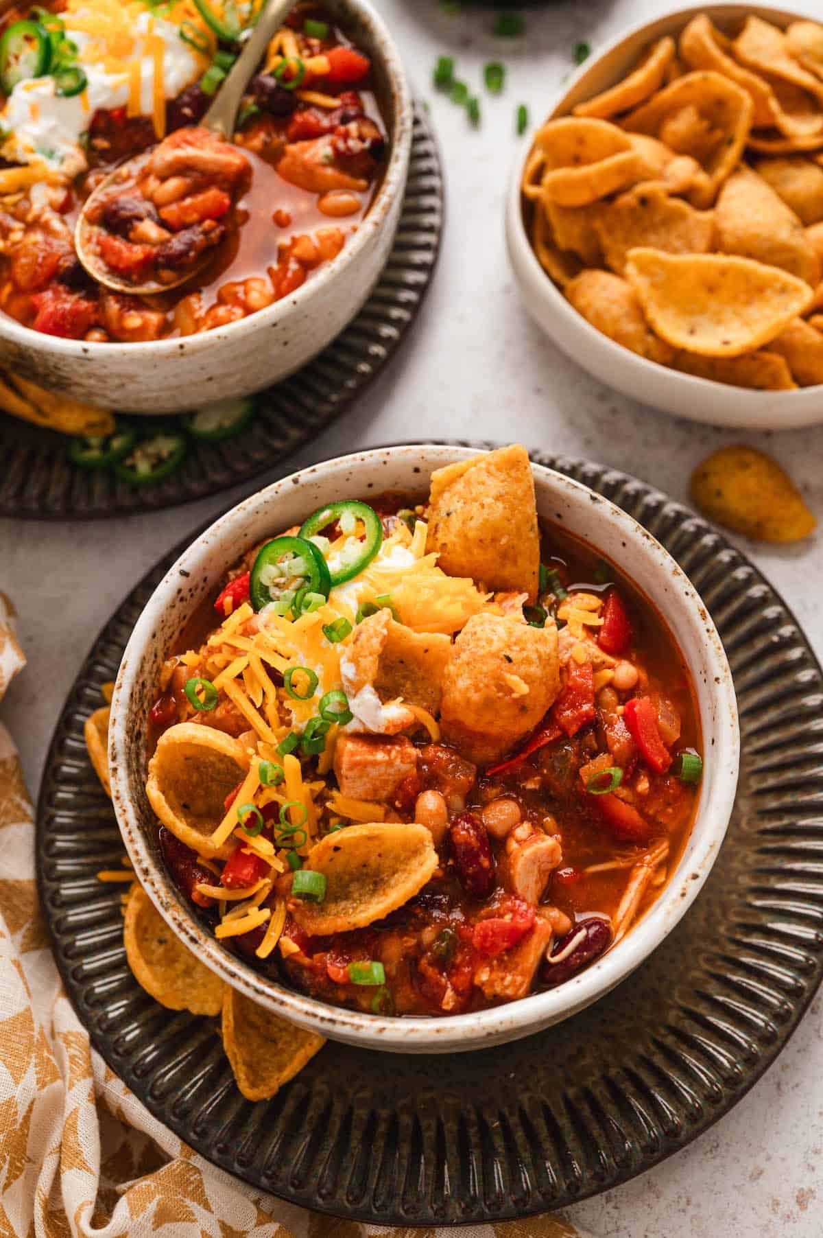 Bowls of chicken chili topped with shredded cheese, sour cream, jalapeño slices, green onions, and corn chips, served as a creative idea for leftover turkey recipes.
