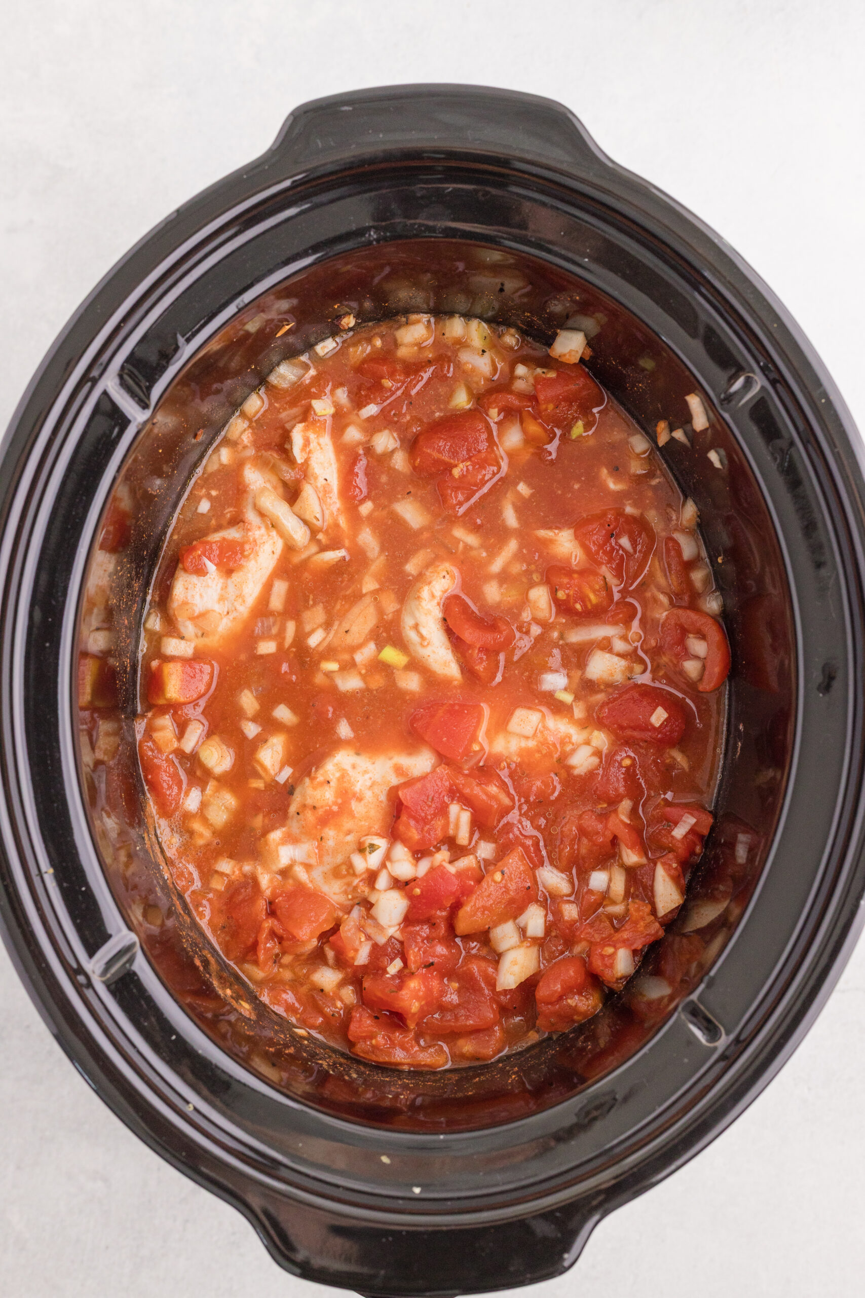 Chicken pieces coated with tomatoes, onion, paprika, and seasonings in a slow cooker.