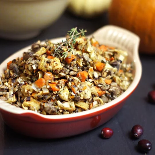 A casserole dish filled with healthy vegetable stuffing, topped with a sprig of thyme and surrounded by fresh cranberries.