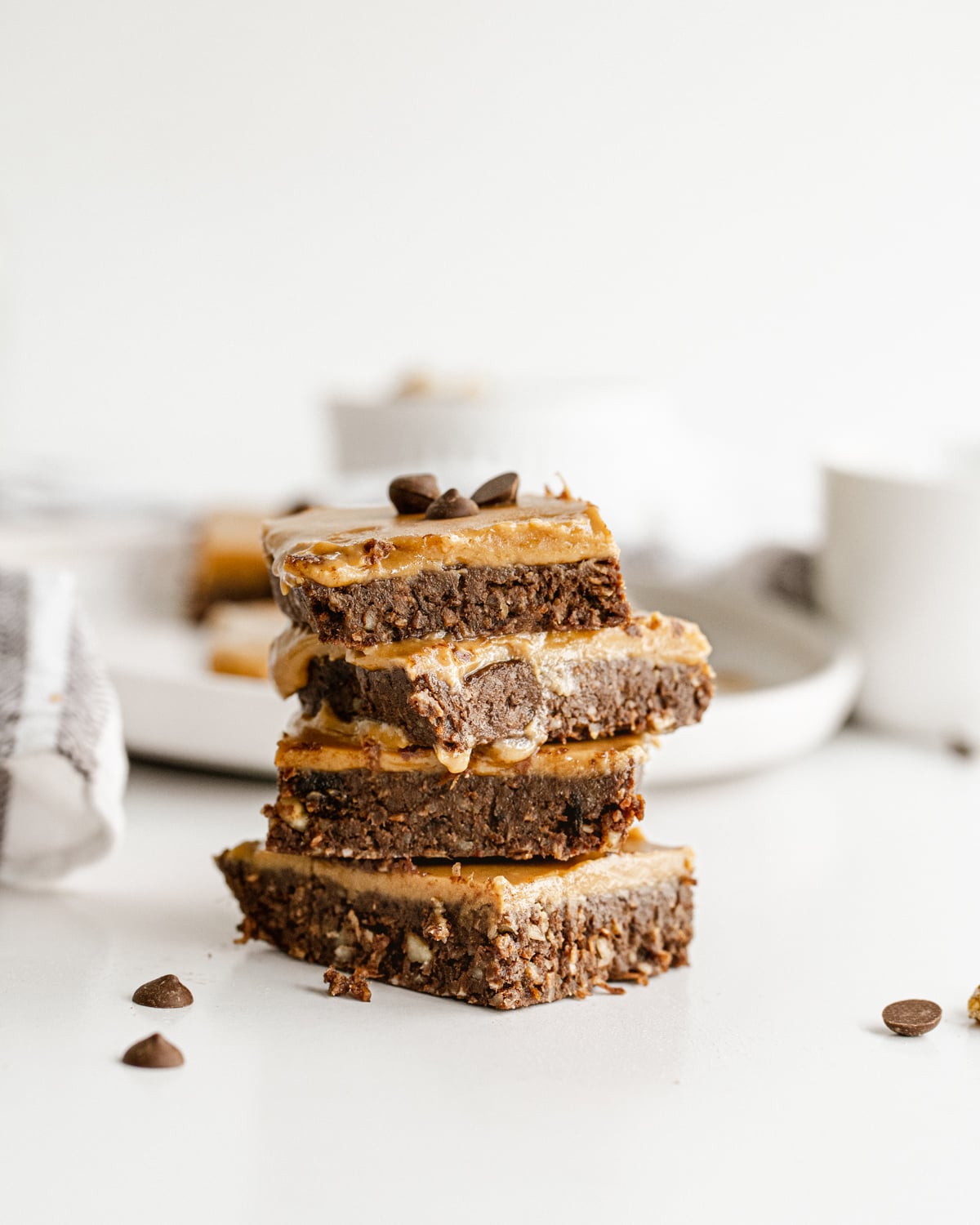 A vertical stack of four no-bake date brownies topped with a smooth caramel layer and scattered chocolate chips.