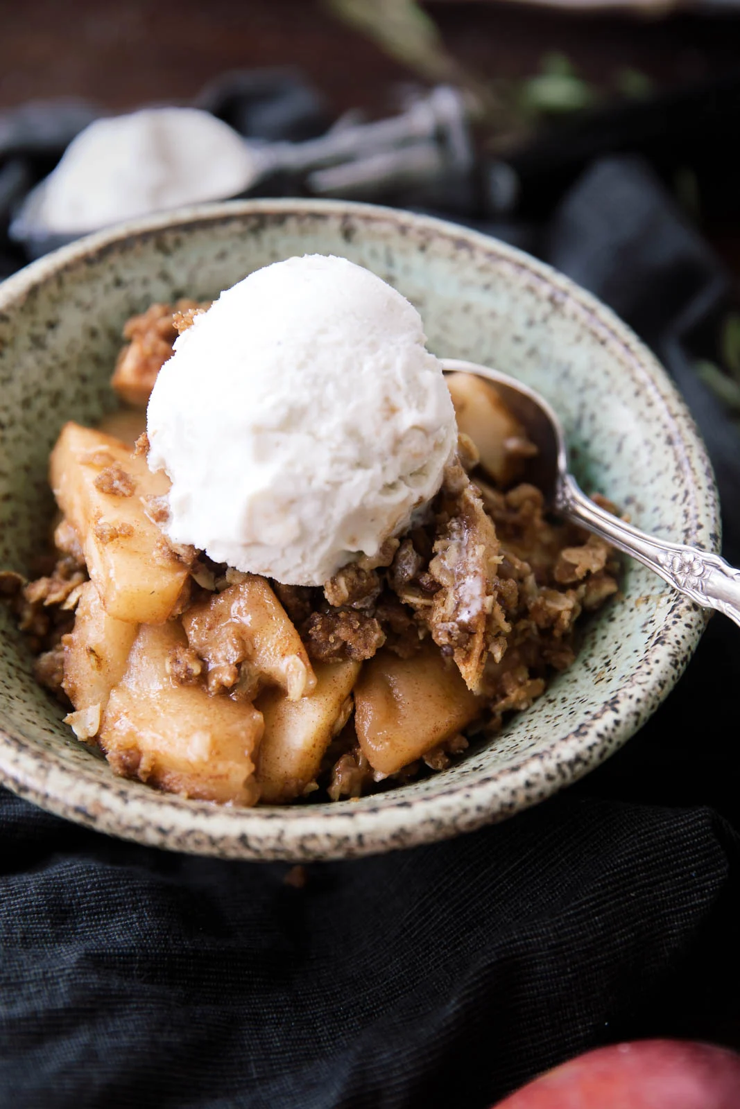 Apple crisp in a bowl topped with a scoop of vanilla ice cream and a spoon, perfect for healthy holiday food.