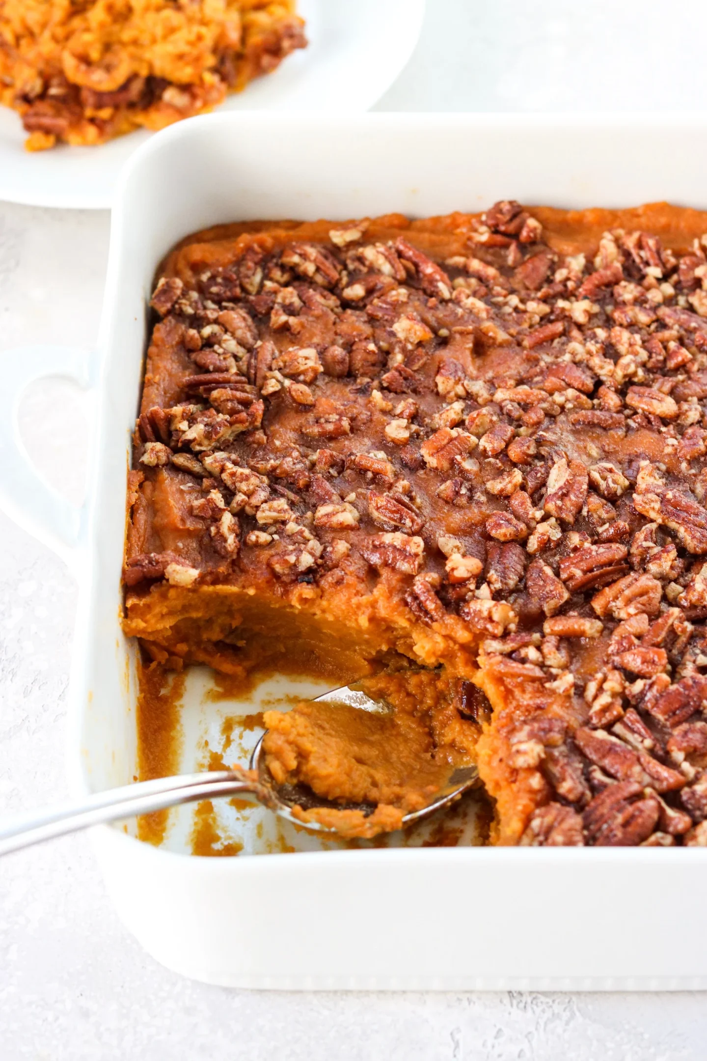 Sweet potato casserole with a pecan topping in a white baking dish, a serving spoon inside this easy Thanksgiving side dish.