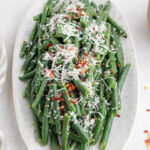 Italian green beans topped with grated Parmesan and red pepper flakes on a serving platter.