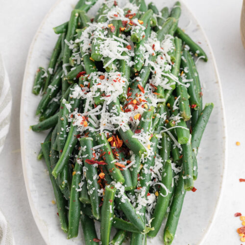 Italian green beans topped with grated Parmesan and red pepper flakes on a serving platter.