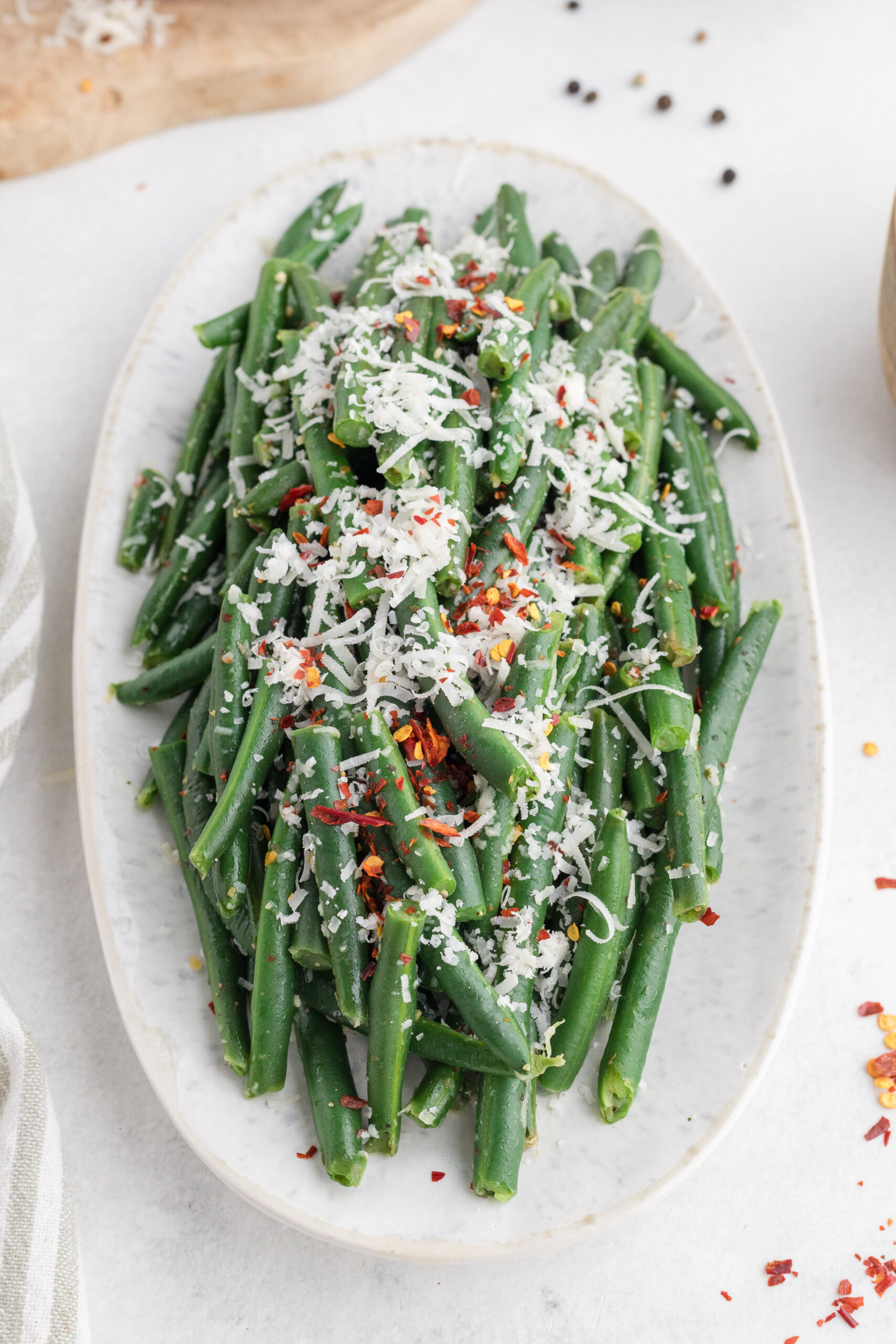 Italian green beans topped with grated Parmesan and red pepper flakes on a serving platter.