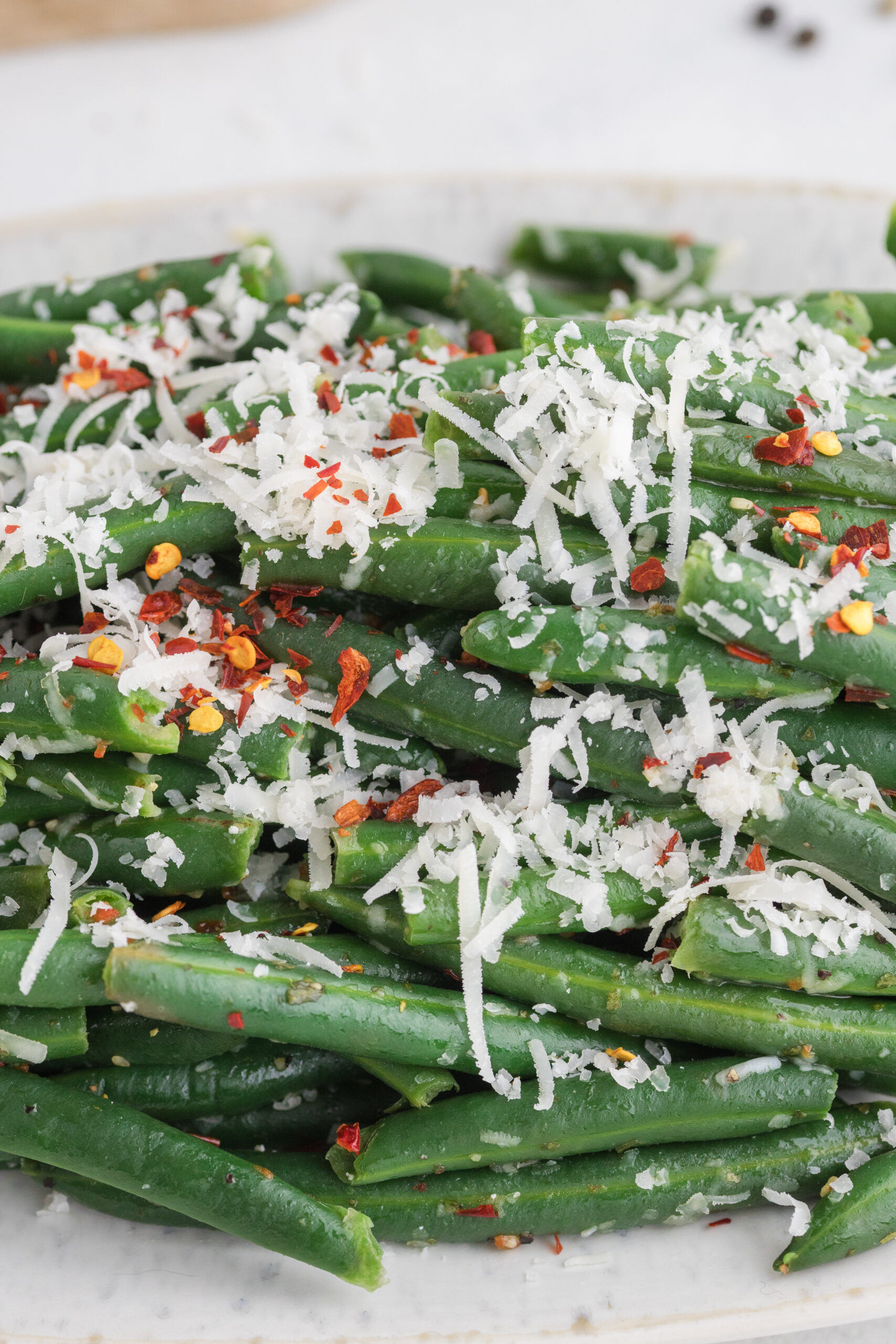 Close-up of tender green beans with grated Parmesan and chili flakes.