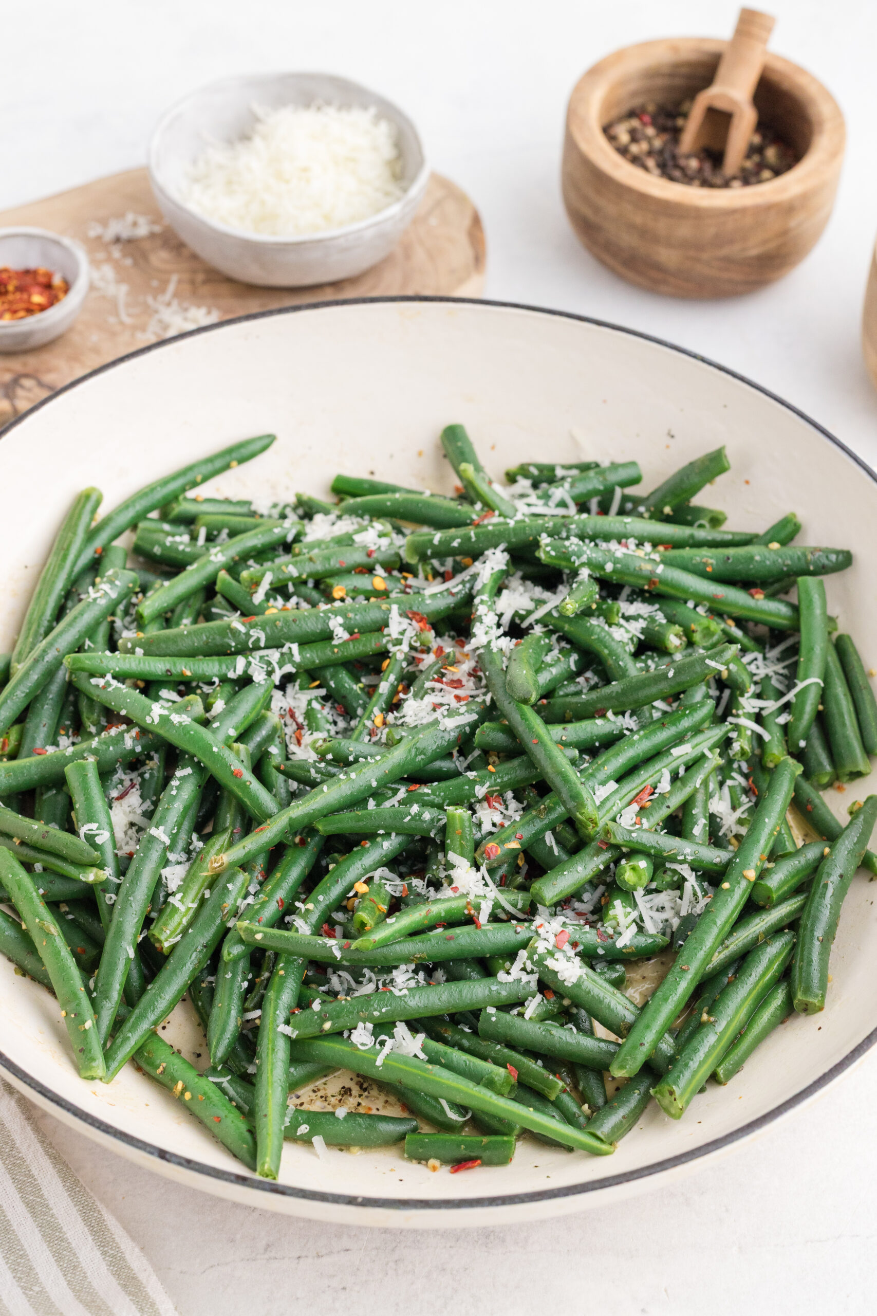 Cooked green beans topped with Parmesan and chili flakes in a skillet.