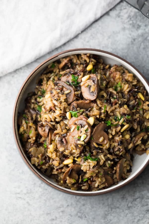 A bowl of mushroom wild rice pilaf garnished with pine nuts and fresh herbs, perfect as a healthy thanksgiving side dish.