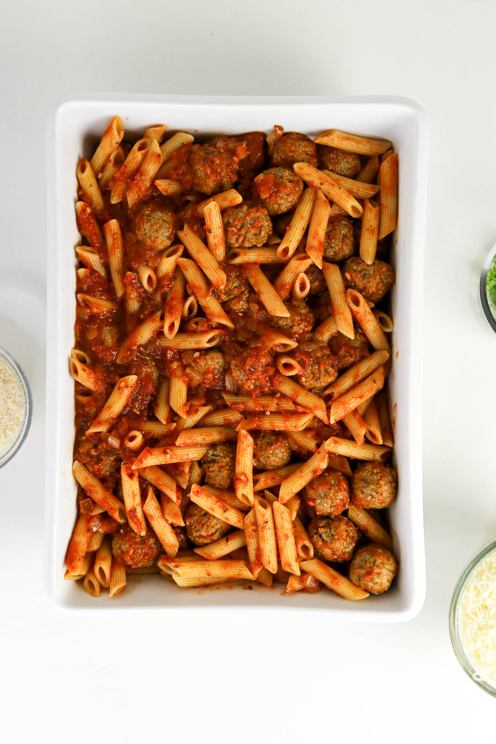 Saucy penne and meatballs spread in a baking dish