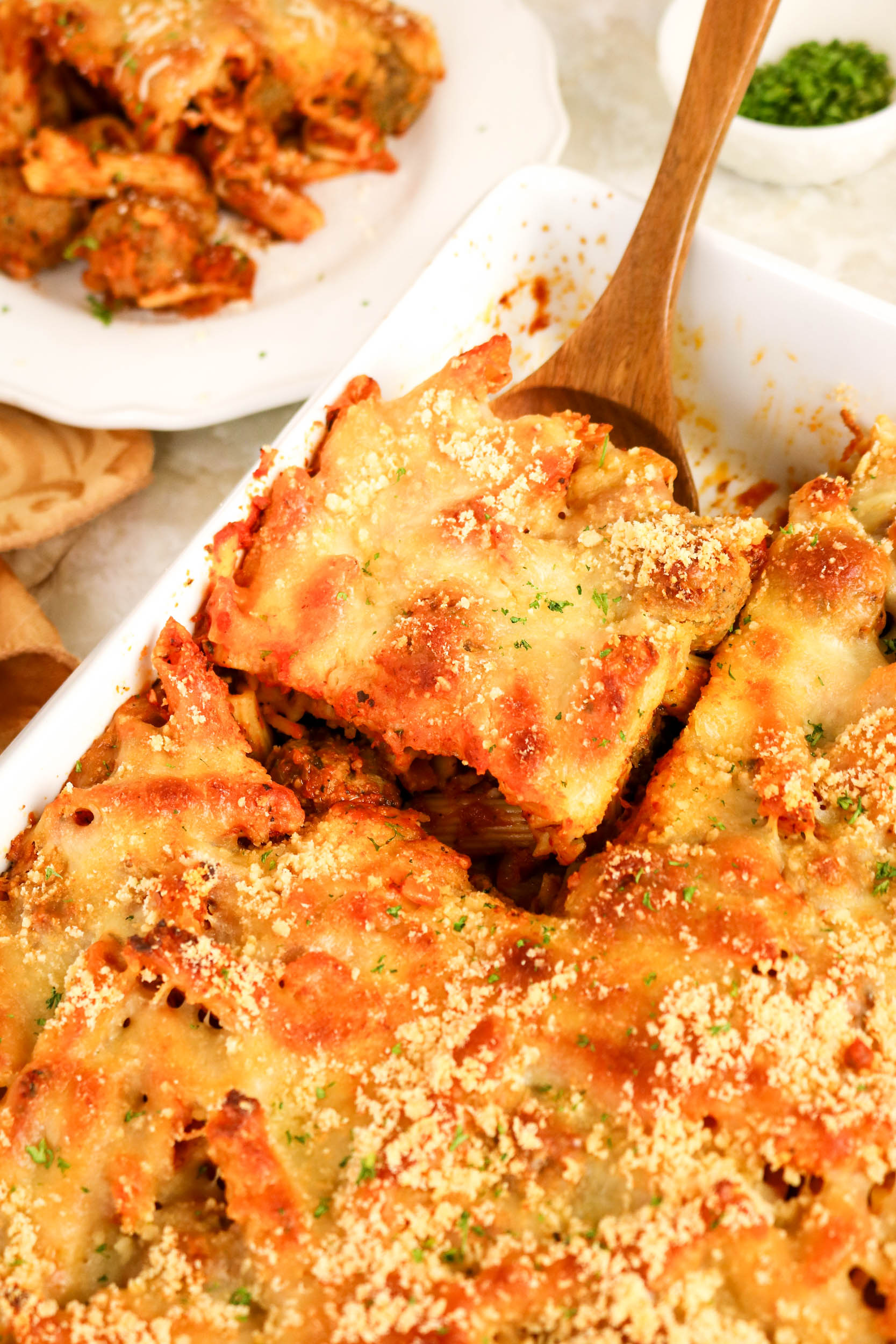 Cheesy meatball casserole being served with a wooden spoon.