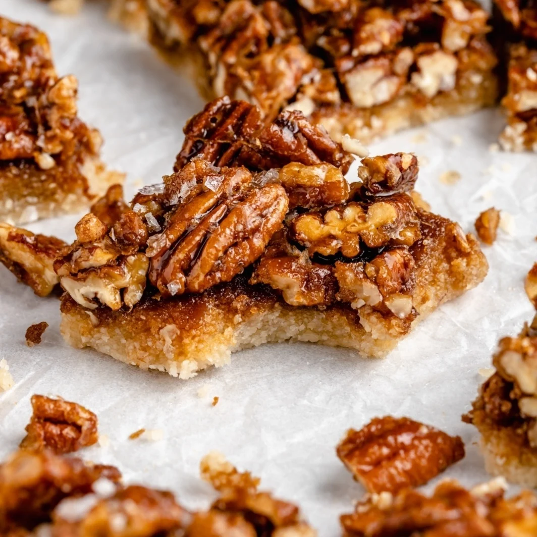 Pecan pie bars topped with coarse salt on parchment paper, representing a healthy Thanksgiving dessert option, with one bar showing a bite mark.