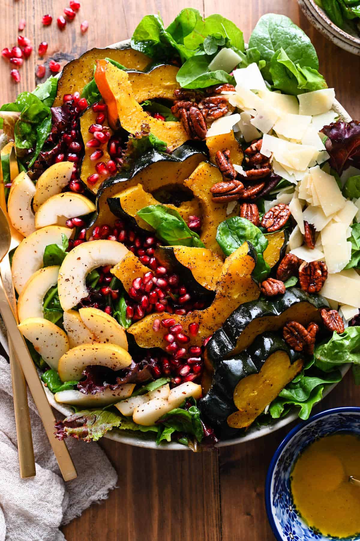A fresh salad of greens, roasted acorn squash, sliced pears, pomegranate arils, pecans, and shaved parmesan, served with a side of dressing as a healthy Thanksgiving recipe.