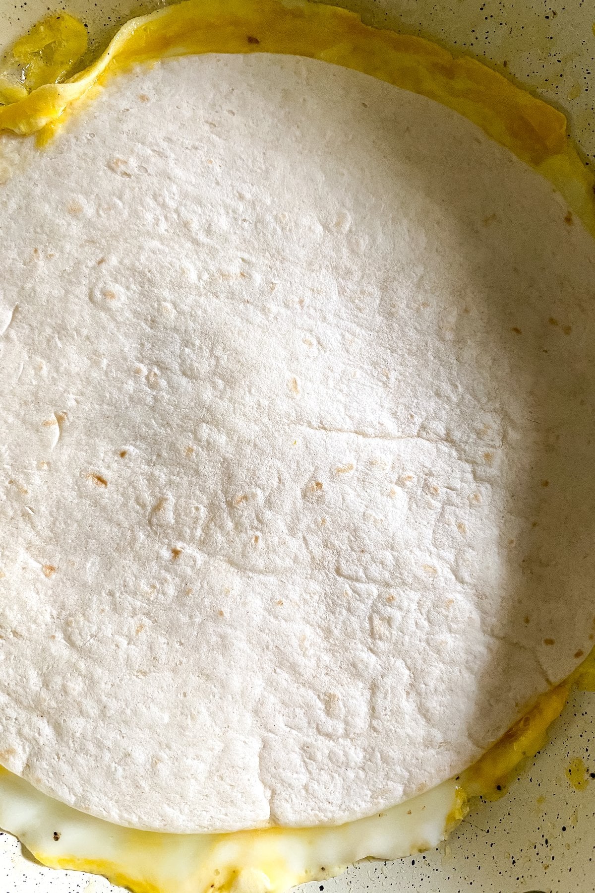 tortilla pressed onto the eggs in a skillet