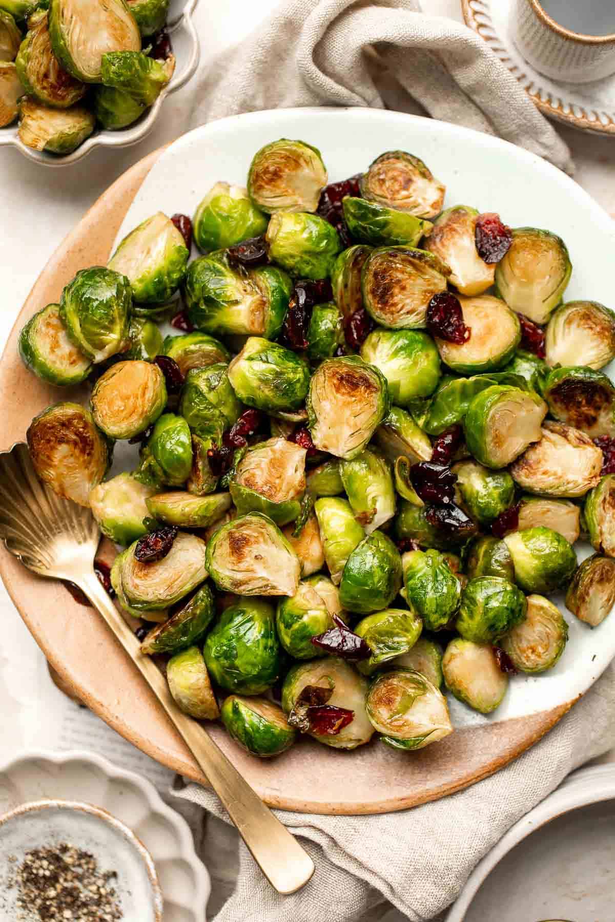 Roasted Brussels sprouts with dried cranberries on a white plate with a gold serving spoon, perfect for healthy holiday food.