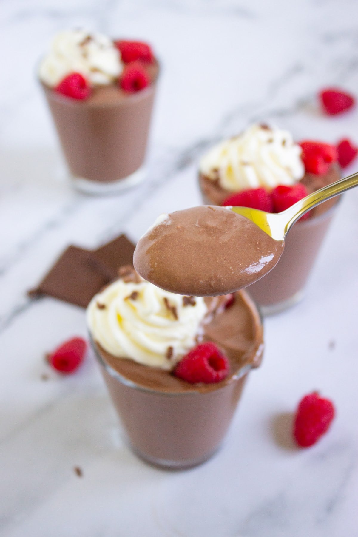 Spoonful lifted from a chocolate peanut butter cottage cheese pudding cup with whipped cream and raspberries.