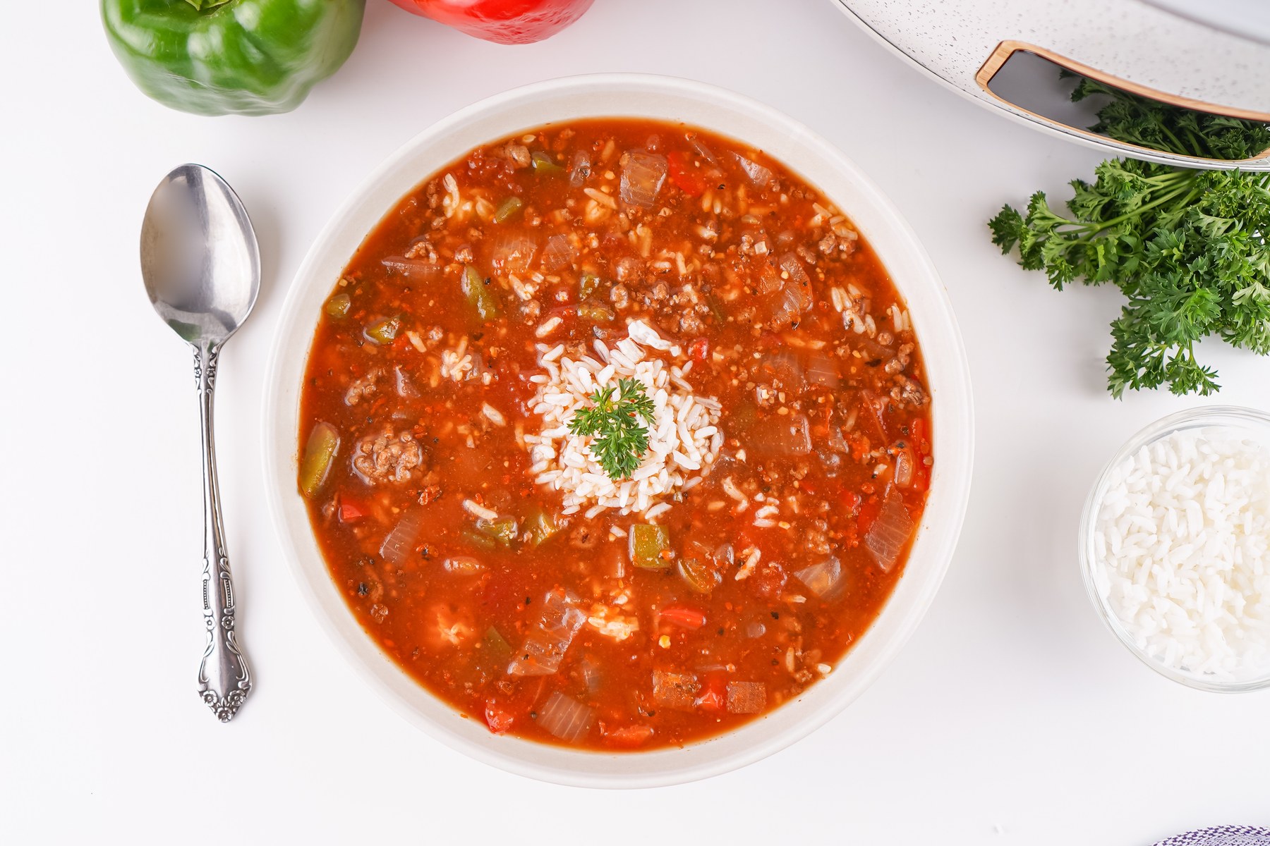 Overhead bowl of stuffed pepper soup with rice, a spoon, and bell peppers.