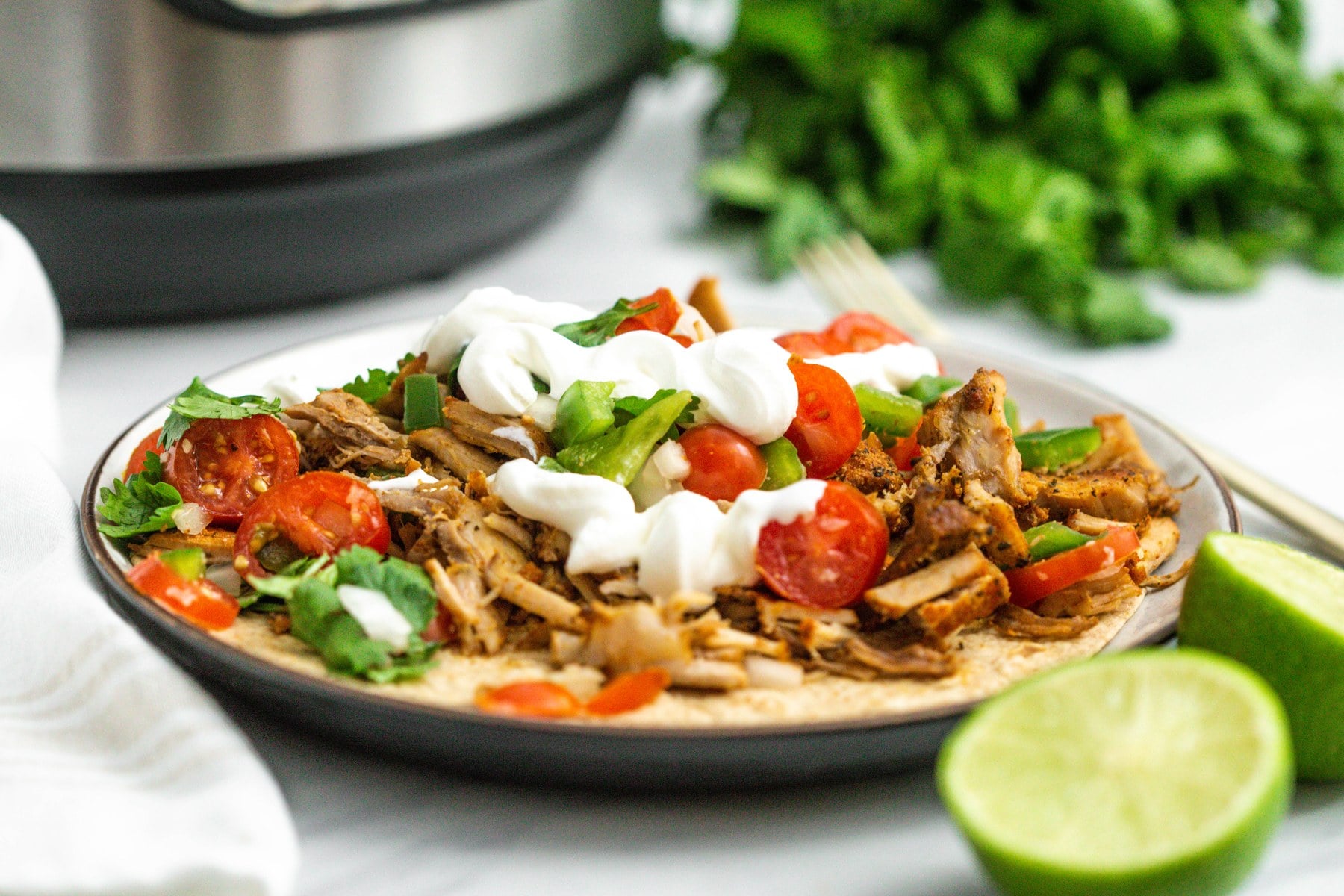Plate of pork carnitas with lime and the Instant Pot behind.